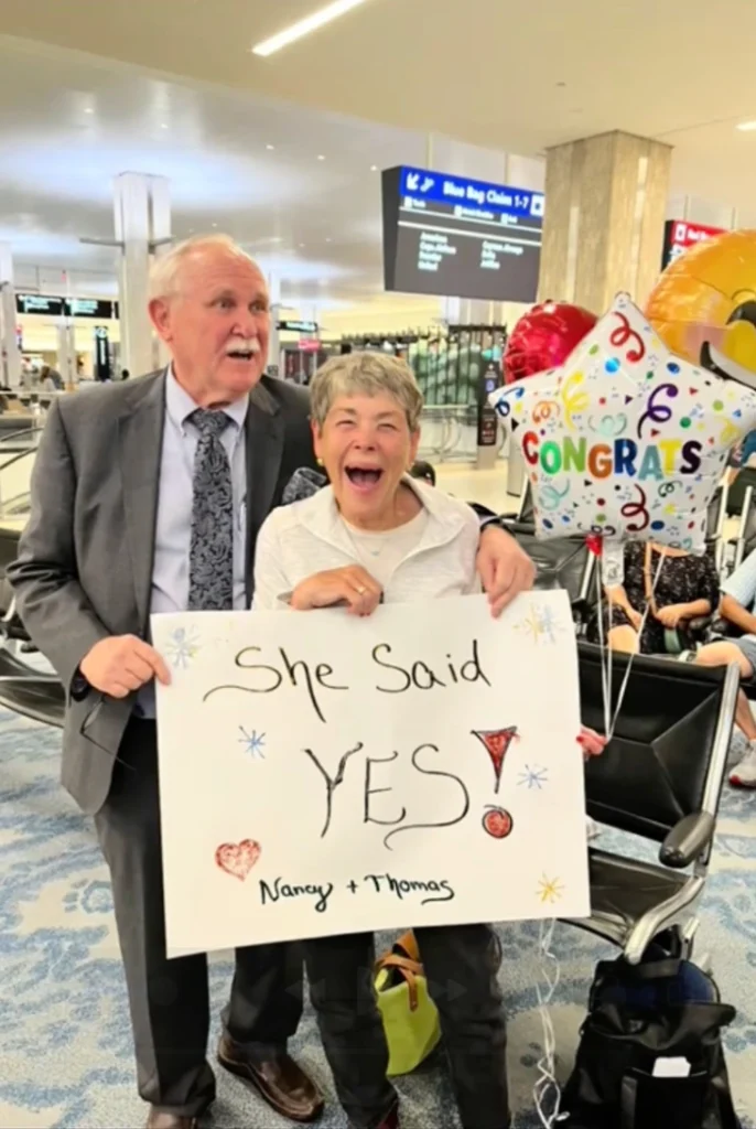 "Newly engaged elderly couple hugging happily at the airport after a romantic proposal."