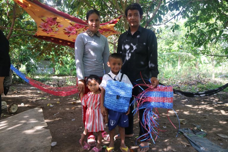 "Cambodian father and son proudly holding the priceless handmade blue raffia school backpack"